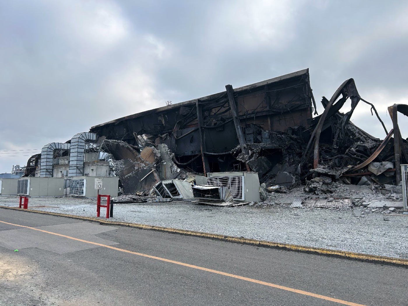 The burned-out remains of the battery building at the Moss Landing energy storage facility, with collapsed roof and charred structural steel.
