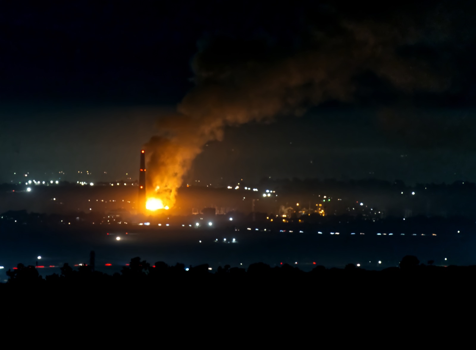A massive fireball and huge column of smoke rising from the Moss Landing battery storage plant at night, visible for miles.